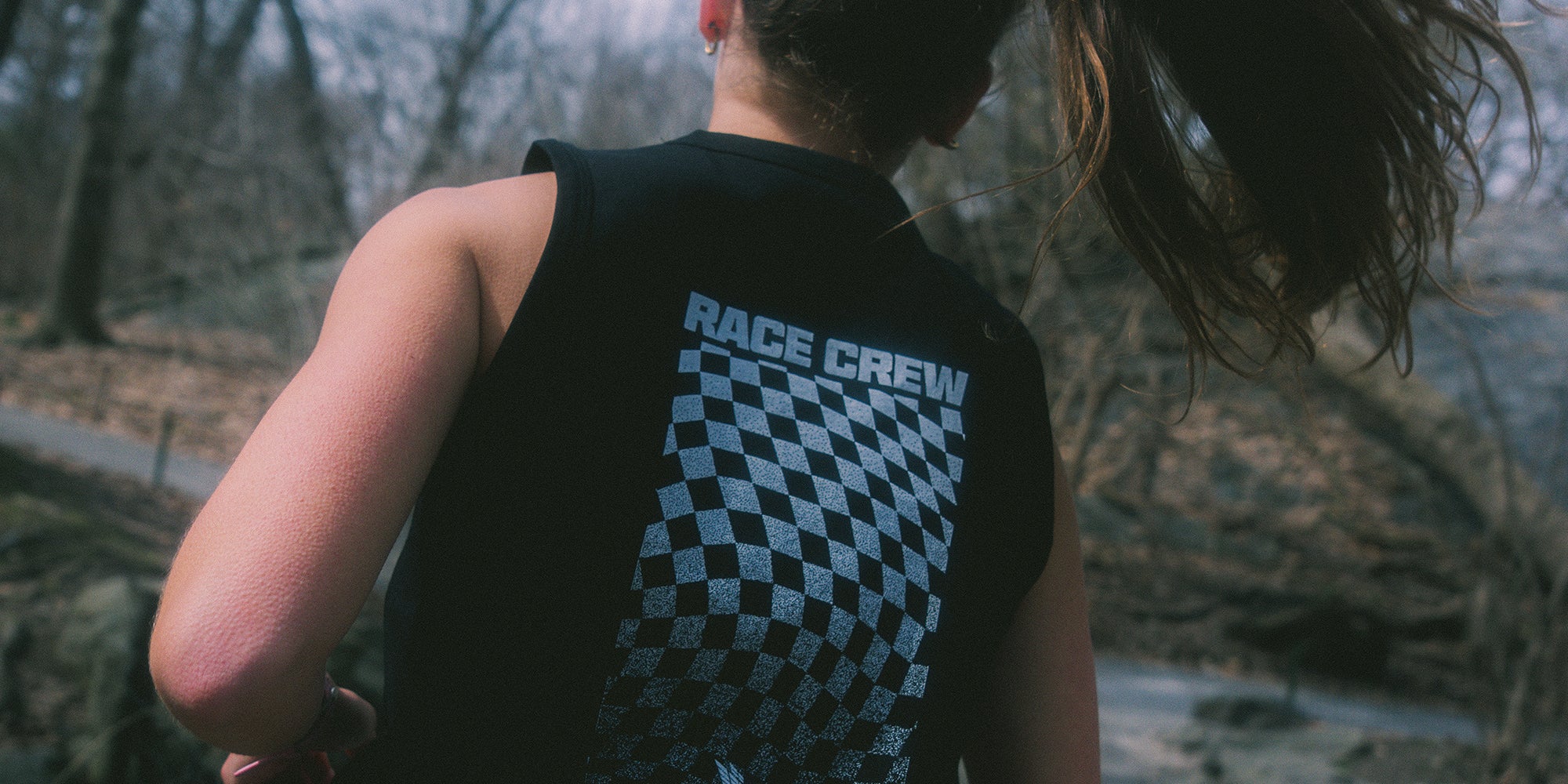 Runner wearing a black sleeveless shirt with 'RACE CREW' text and checkered pattern outdoors.