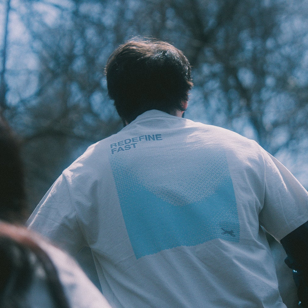 Person running and wearing a white shirt with a blue logo Redefine fast artistic print in a forest setting.