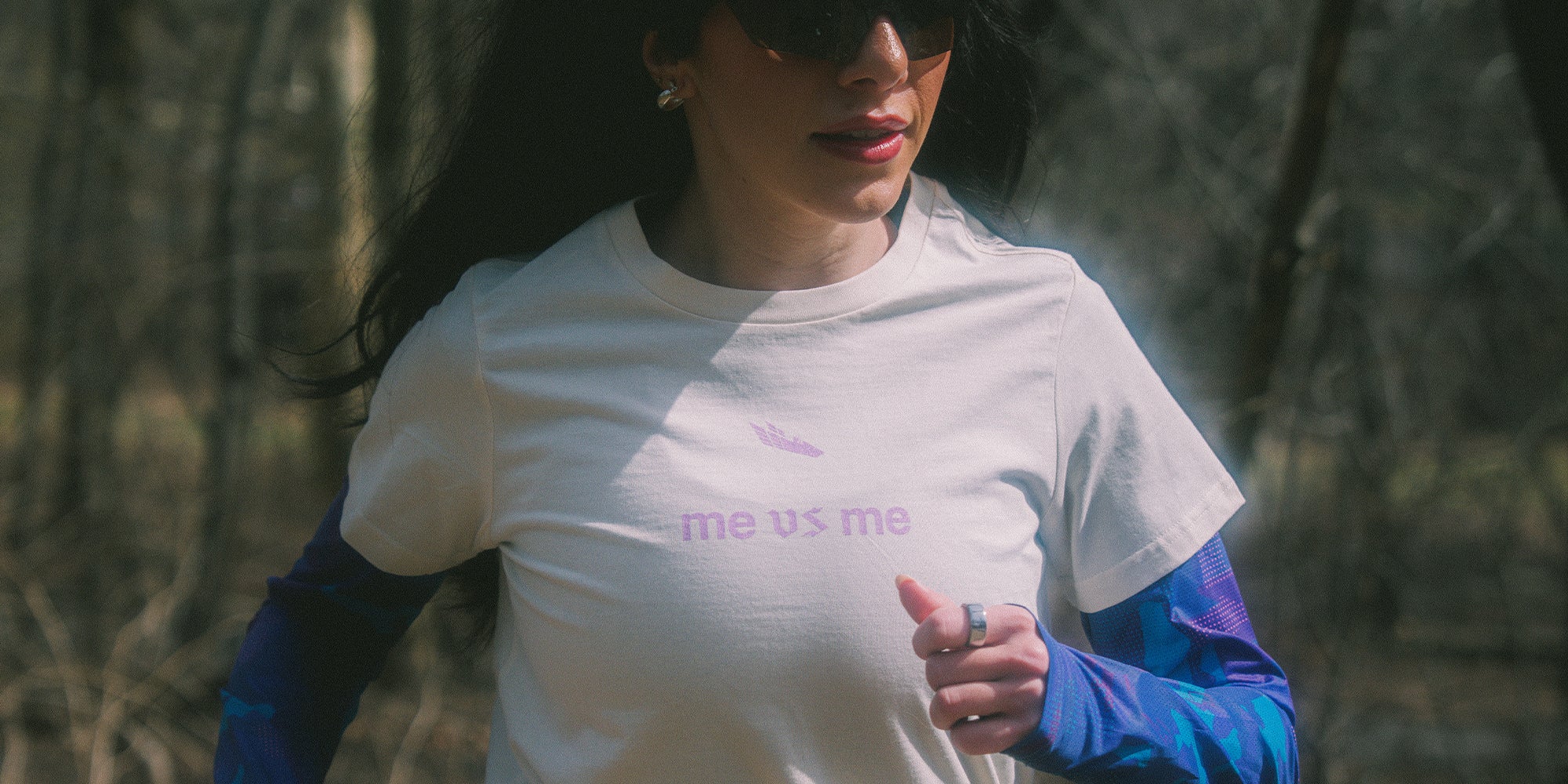 Female Athlete wearing an off-white shirt with "me vs me" logo on the front in purple gothic font.